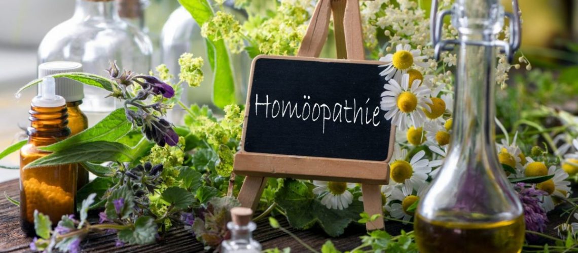 Verschiedene Heilpflanzen und Fläschchen mit Schild: Homöopath